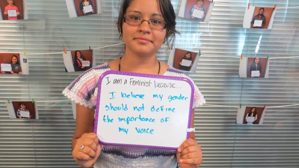 Person holding a hand-written sign that reads, I am a feminist because...I believe my gender should not define the importance of my voice.